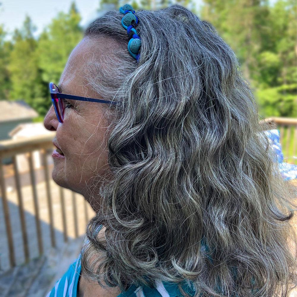 A woman wearing the AtlanTick Lava Hair Band outdoors, featuring durable nylon cording and lava beads designed to absorb Tick Attack™ Botanical Insect Repellent for a fresh, natural scent. Versatile for both fashion and function.