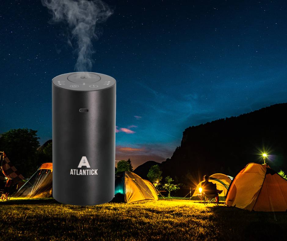 The AtlanTick Portable Air Infuser releases a fine mist of essential oils against a stunning night sky, surrounded by illuminated tents in a scenic camping area. Designed for outdoor adventures, the sleek black infuser helps create a fresh, aromatic atmosphere while blending seamlessly into the natural surroundings.