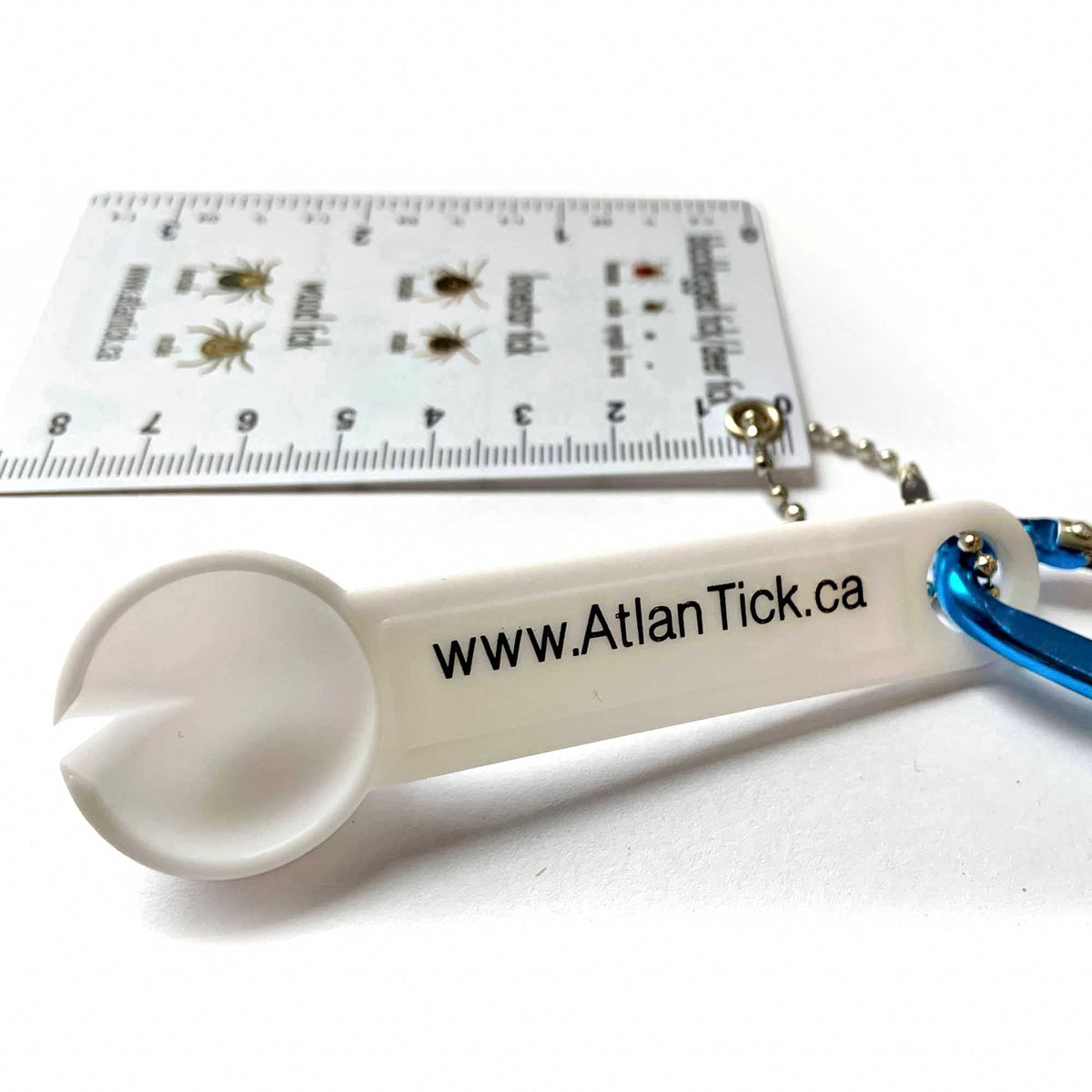 Close-up of the AtlanTick Tick Scoop Remover, a white plastic tick removal tool with a scoop design, attached to a blue carabiner and a tick identification ruler.
