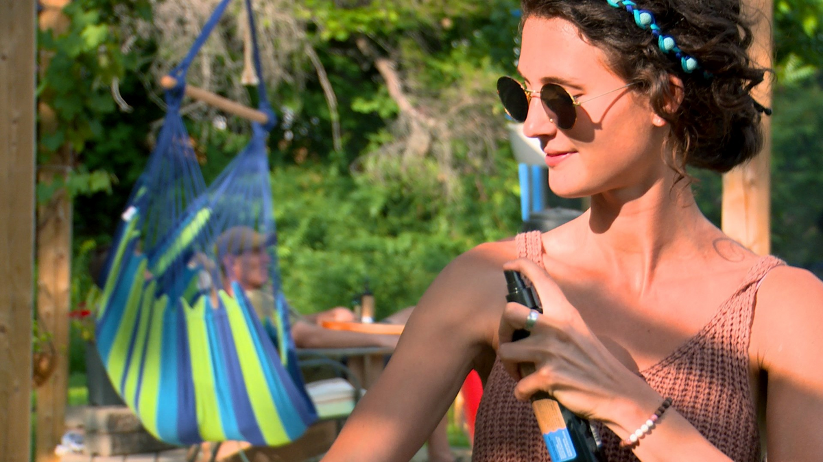 A woman outdoors spraying Tick Attack™ Botanical Insect Repellent onto her arm. Showcasing the simple, effective application of the DEET-free formula for natural tick protection.